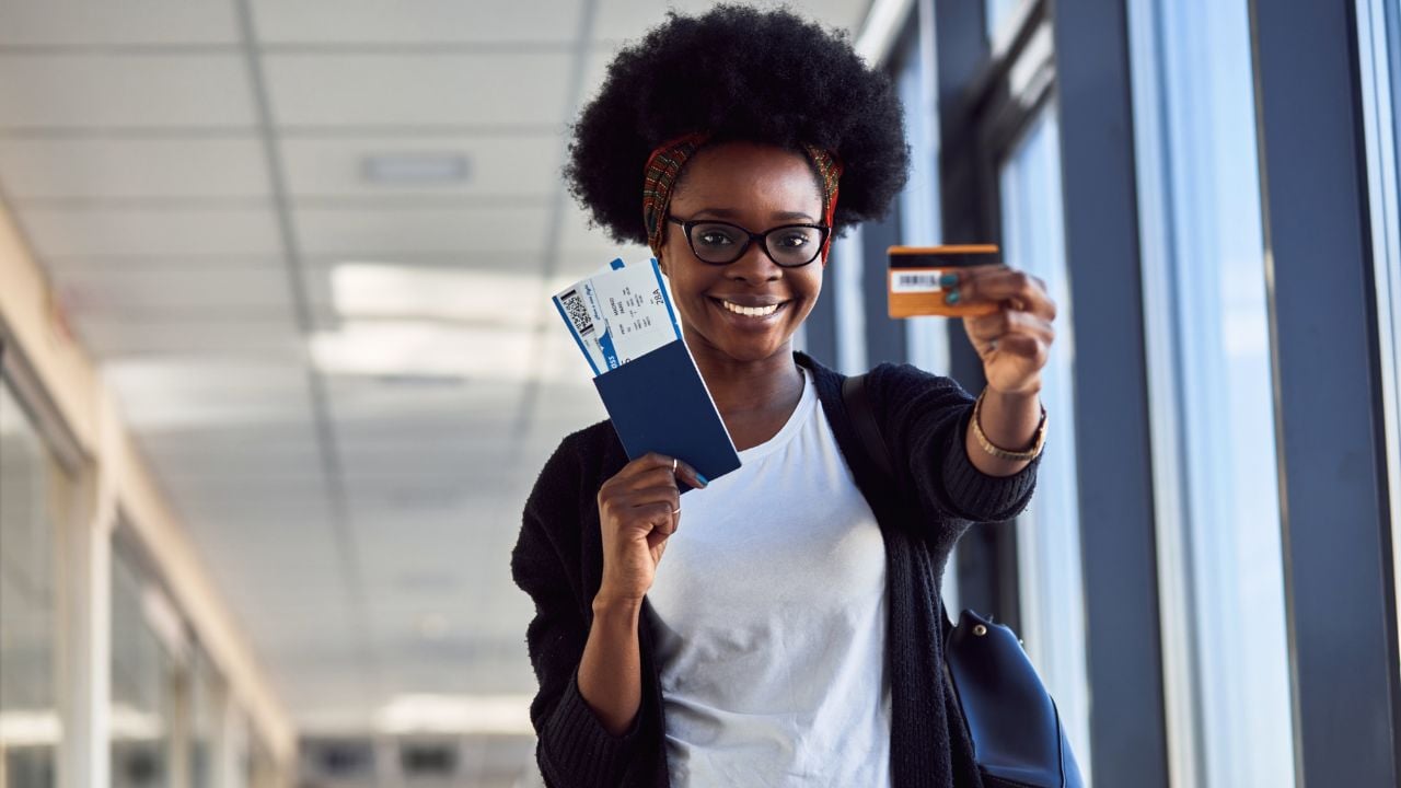 Young African American female passenger in casual clothes at airport holding tickets and credit card.