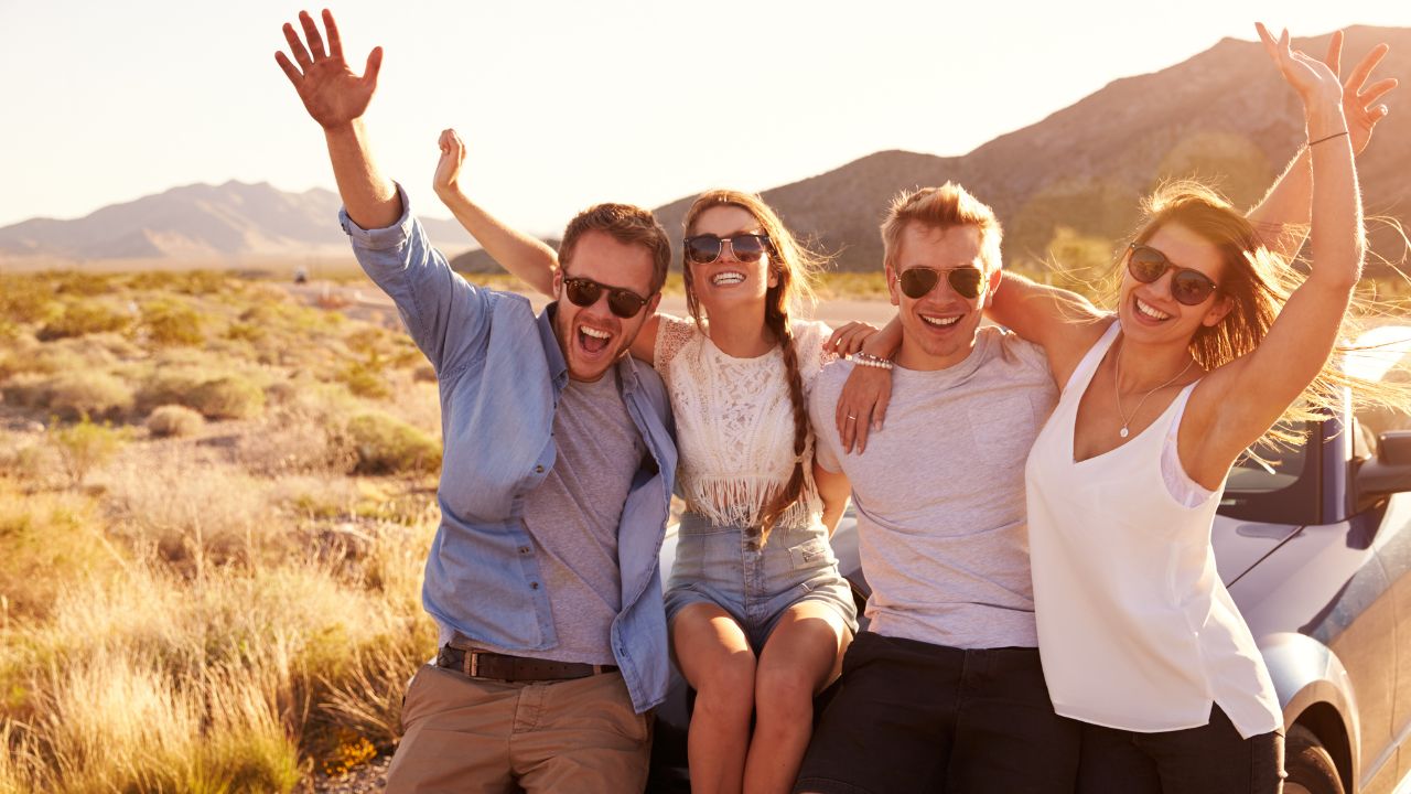 Friends on a road trip sitting on the hood of a convertible car