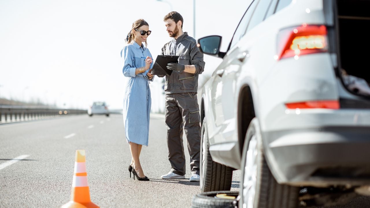 Road assistance worker helping a woman near a broken car on the highway