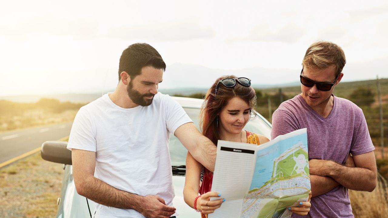 Friends on a road trip reading a map by their car