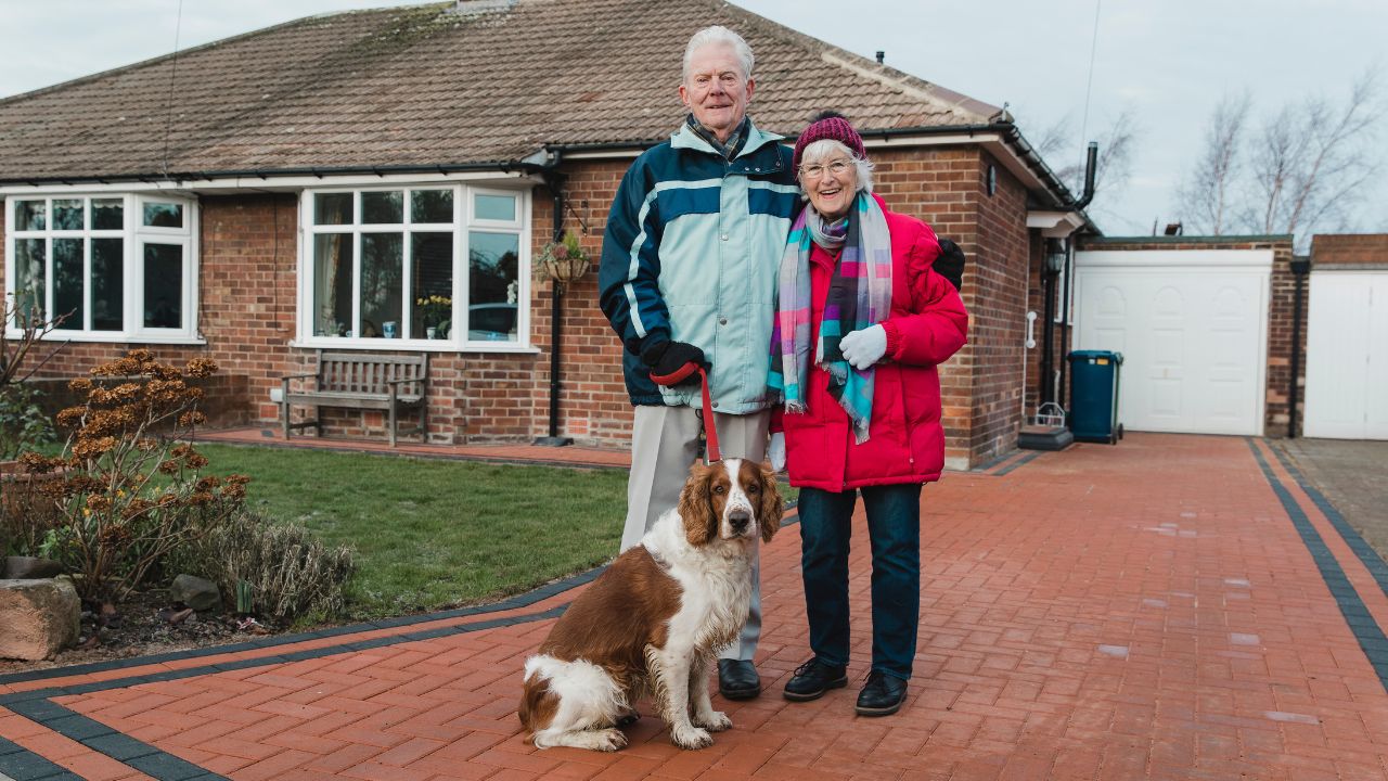 Portrait of a senior couple and their pet dog in the front yard of their house.