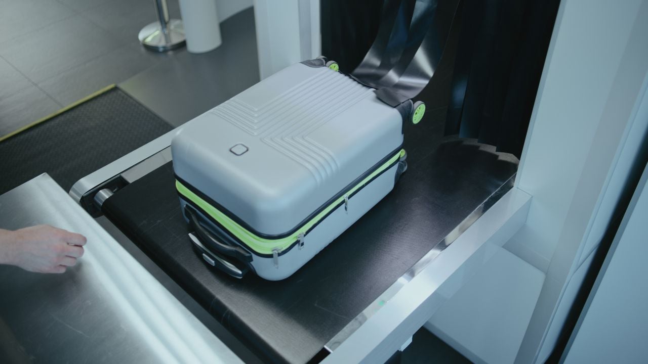 Passenger collecting a suitcase from an airport security conveyor belt.