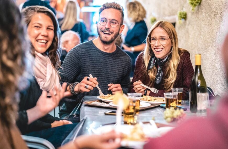 Young friends having fun drinking white wine at street food event - Happy people eating local meal plates at open air restaurant together - Travel and dinning life style concept on bulb light filter
