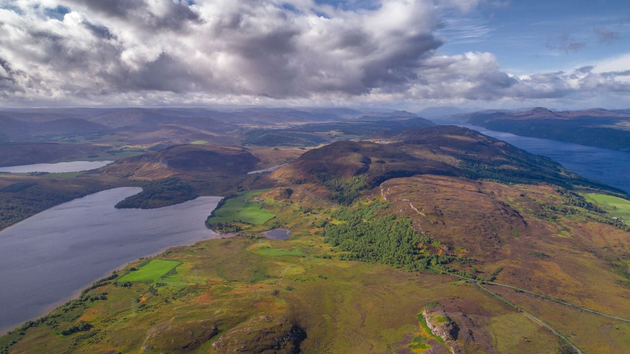 Horizontal aerial wide angle view of lochs, clouds, casted shadows above the highlands of Scotland, green covered mountain tops beautiful layers scenic landscape view sunny foreground hazy background.