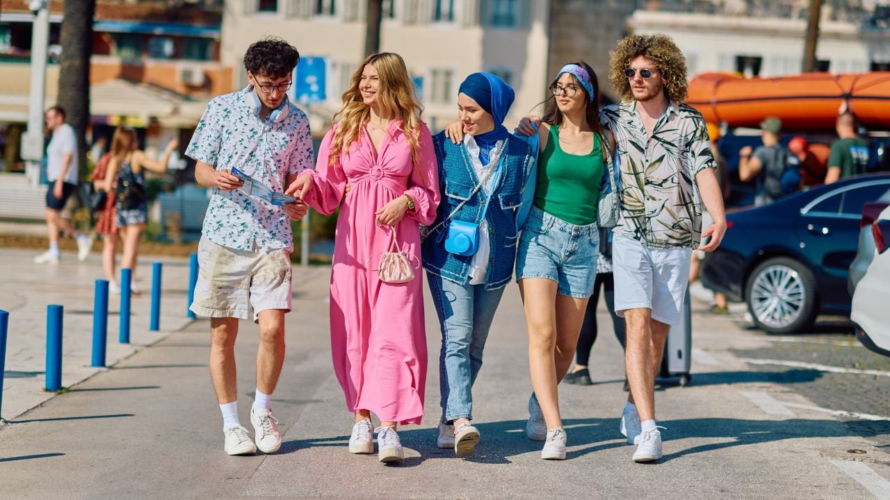 A diverse group of tourists, dressed in summer attire, strolls through the tourist city with wide smiles, enjoying their sightseeing adventure