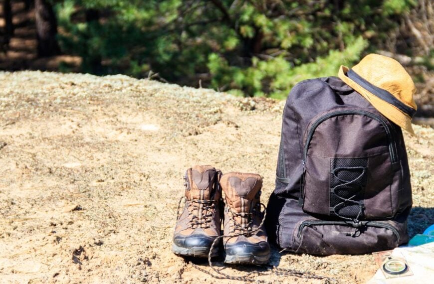 Tourist backpack with hiking boots, hat, compass and map on the glade in pine forest. Trekking hike gear equipment. Travel concept