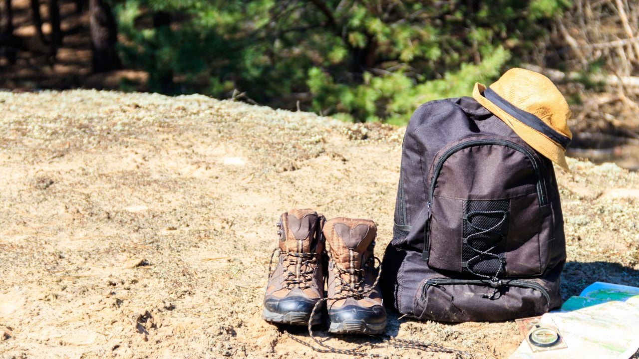 Tourist backpack with hiking boots, hat, compass and map on the glade in pine forest. Trekking hike gear equipment. Travel concept