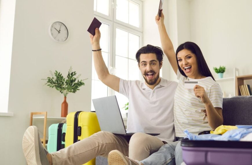 Ready for vacation. Happy young couple in love having fun on couch at home glad they've packed travel bags, picked airline online and bought tickets that soon will get them to trip destination abroad