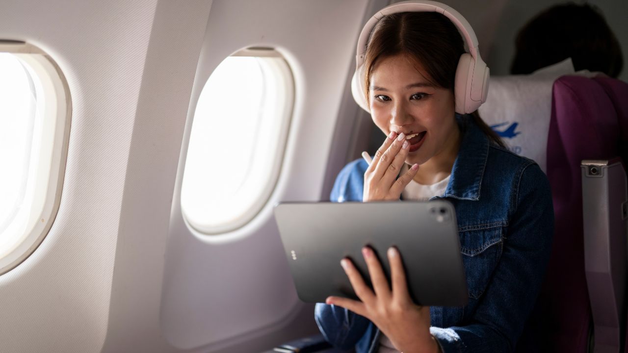Young woman smiling while watching a movie with headphones on an airplane