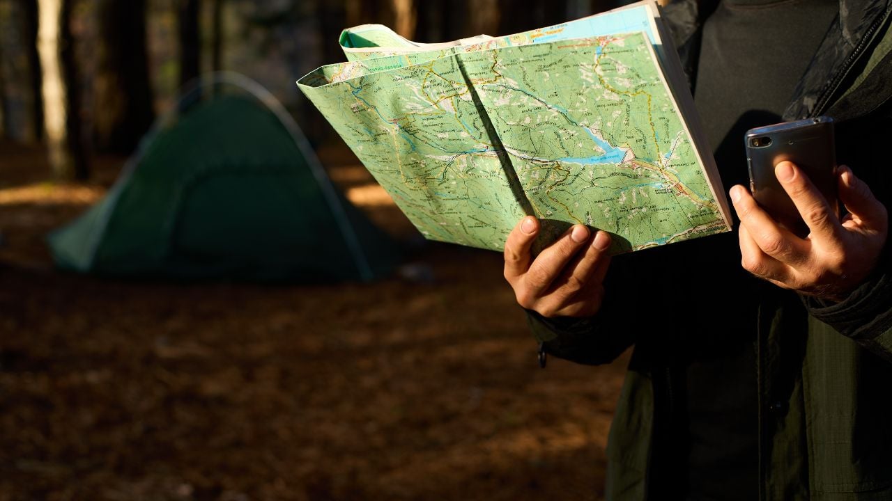 Traveler using a map and phone near a campsite