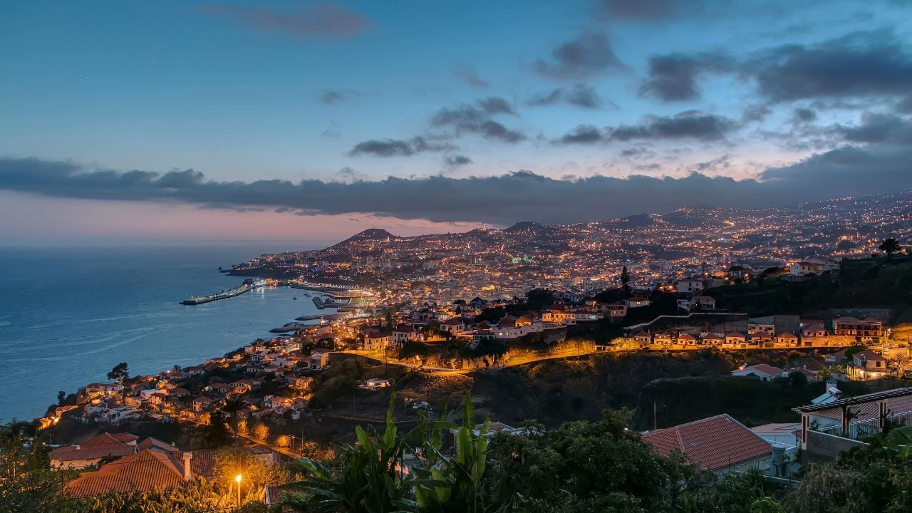 Island landscape after sunset panoramic aerial view to Funchal day to night transition, Madeira, Portugal timelapse. Port in harbor with evening illumination and city lights