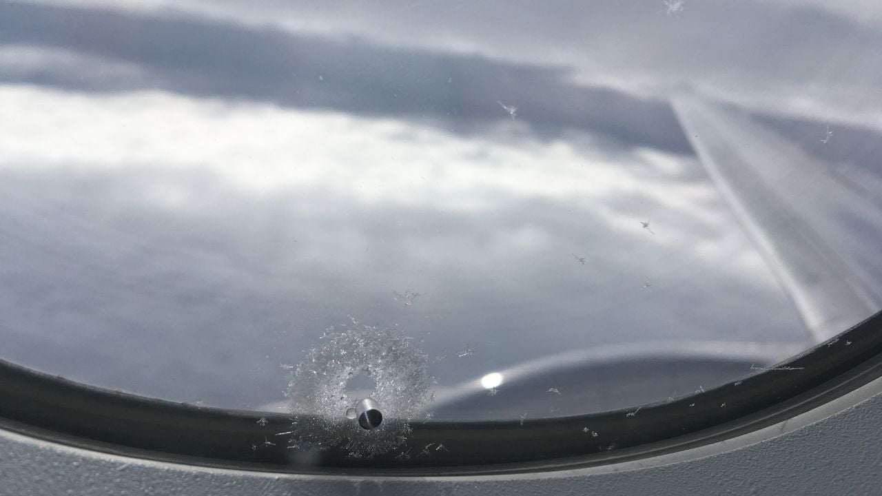 Close-up of a small hole in an airplane window assembly.