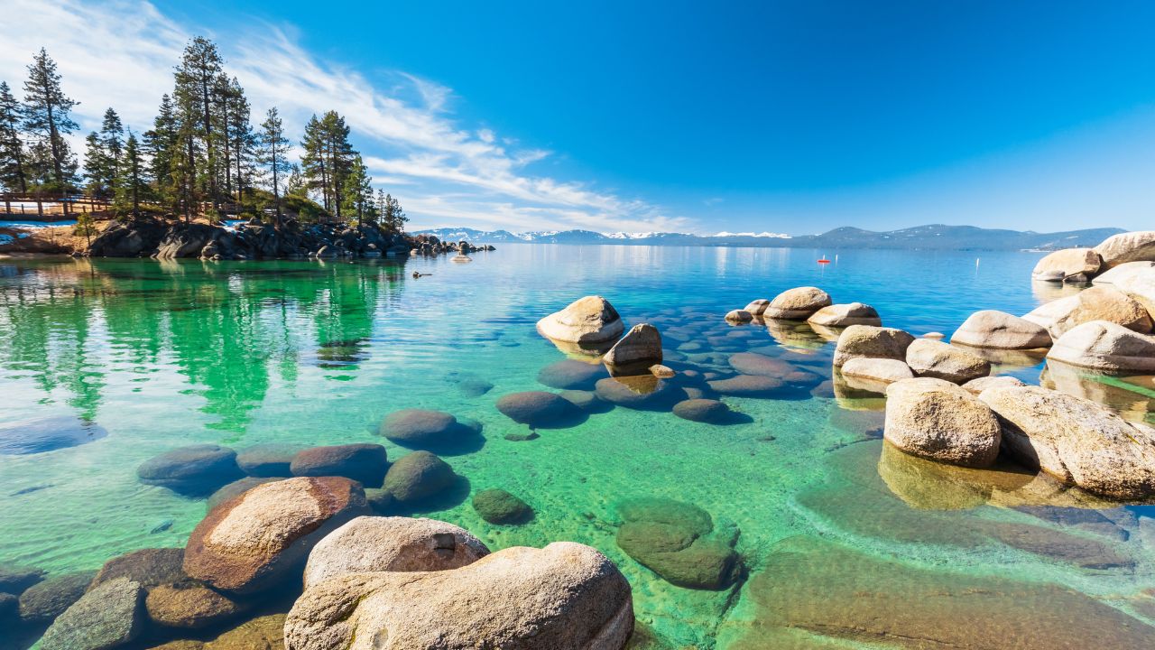 Lake Tahoe rocky shoreline in sunny day, beach with blue sky over clear transparent water