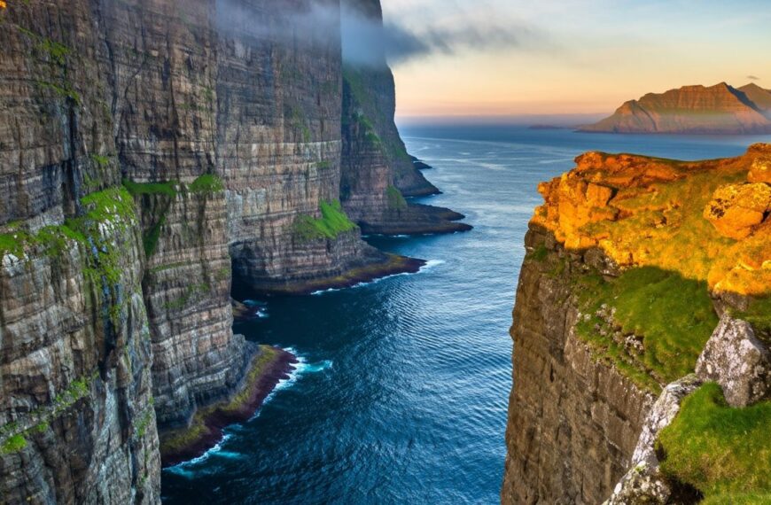Faroe Islands coastal landscape with steep green cliffs, ocean waves, and dramatic cloudy sky. Remote North Atlantic scenery with rugged nature and minimal human presence, ideal for travel and nature themes.