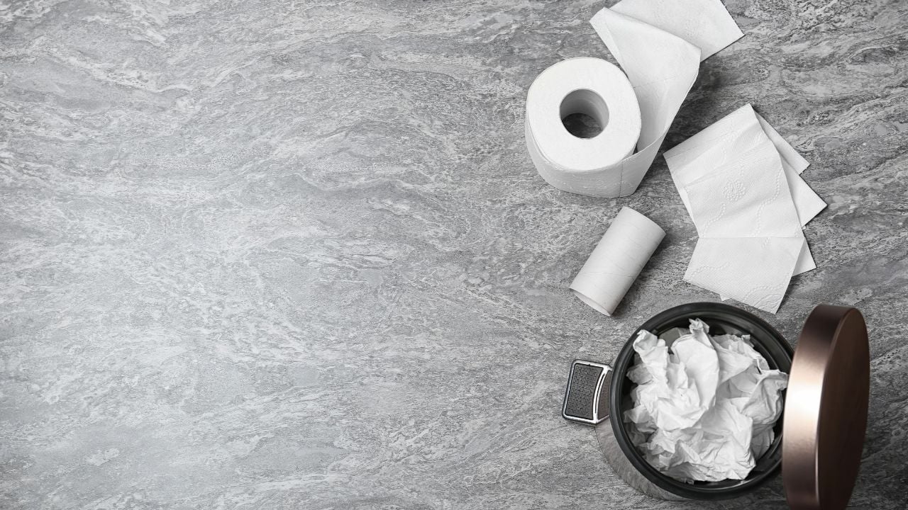 Trash bin with used toilet paper and a new roll on a grey background