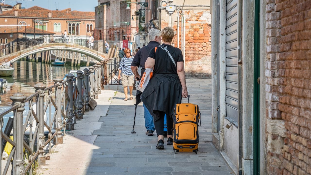 Venice, Italy - May 29 2023: unidentifiable tourist woman with a luggage trolley walking near a water canal in Venice, Italy.
