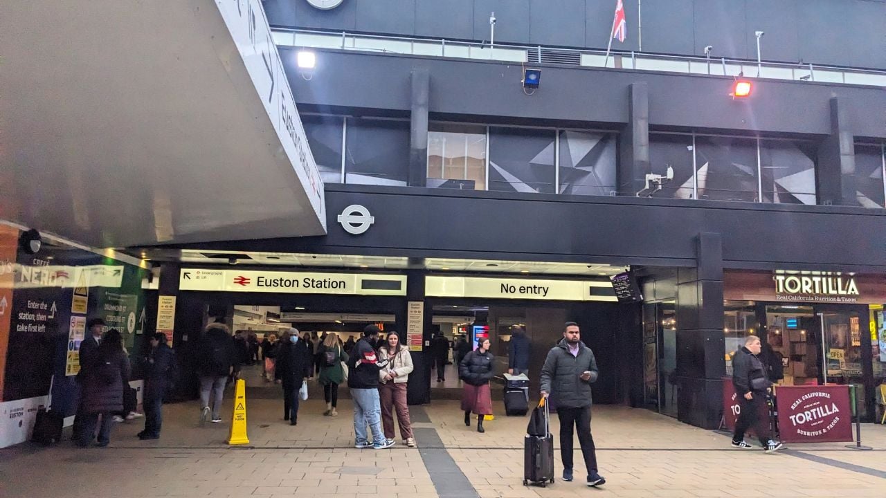 London, United Kingdom - March 07 2026: Commuters with luggage and pedestrians walk past the modern entrance of Euston Station, featuring signage and a London Underground roundel in the daytime