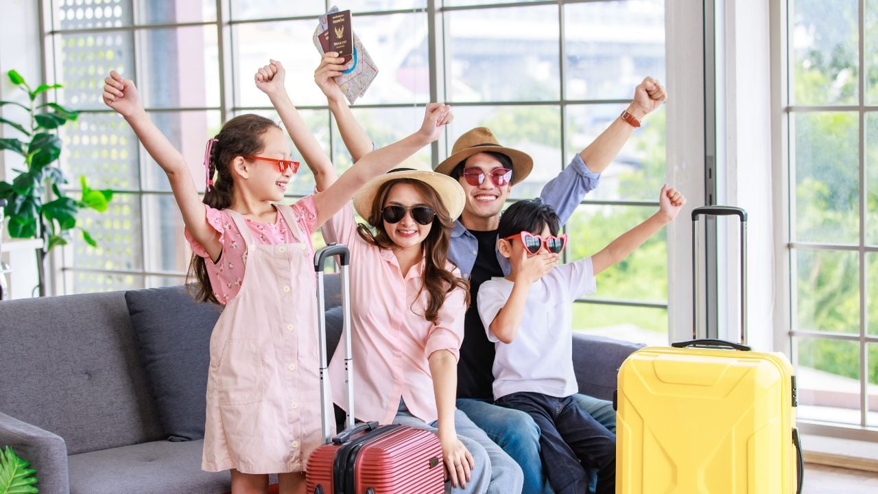 Asian cheerful happy family mom dad son and daughter wearing sunglasses and hat with two trolley luggages raising hands smiling celebrating holiday together ready for traveling vacation road trip.