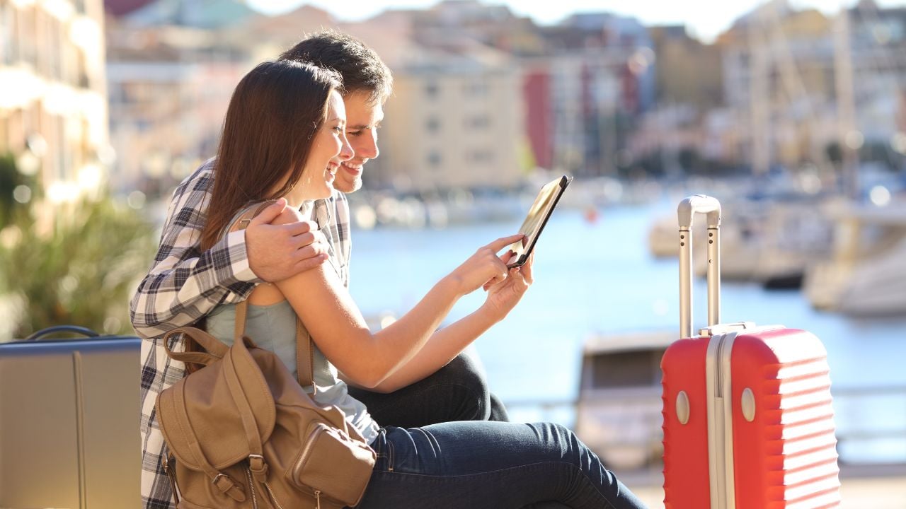 Side view portrait pf a happy couple of tourists consulting a tablet on vacation