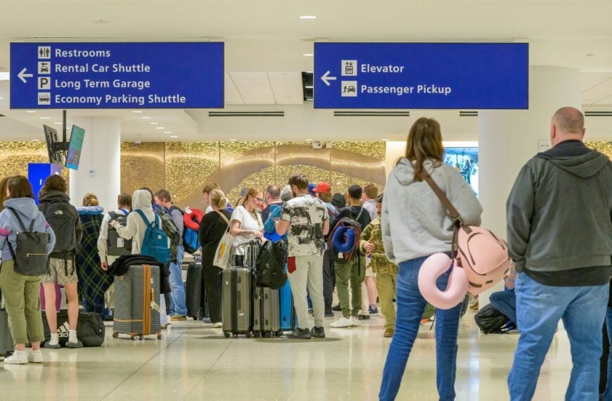 Travelers wait in long lines with luggage at a crowded airport terminal, highlighting how peak holiday periods can disrupt schedules, increase wait times, and make trips more stressful.