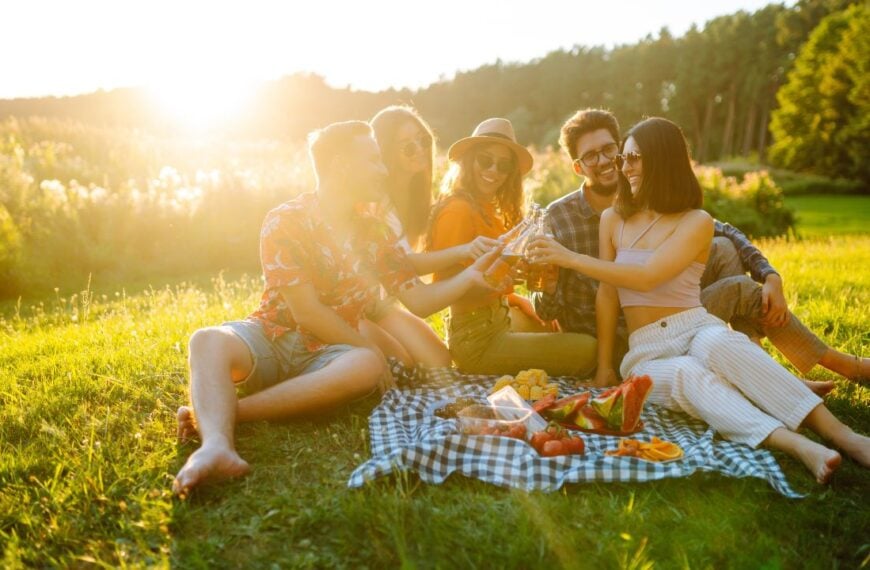 Group of happy friends cheers and drink beers on in summer park. Vacation, picnic, friendship or holliday concept.