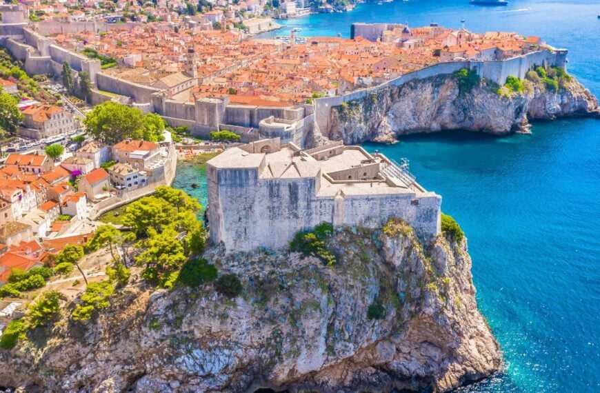 A stunning view from behind Fort Lovrijenac in Dubrovnik, Croatia, capturing the fortress’s massive stone walls, the UNESCO-listed Old Town with its historic architecture, and the scenic marina.