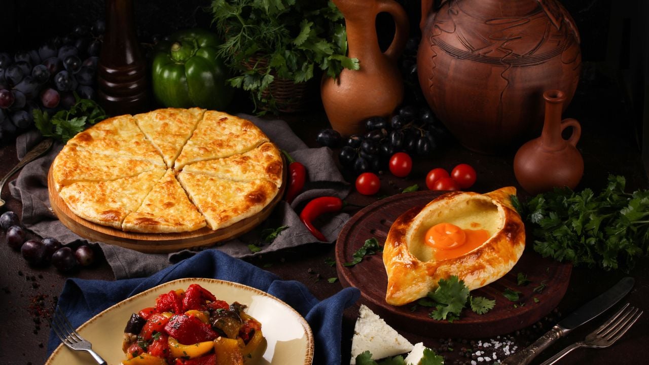 Georgian table with Adjarian khachapuri, wine, vegetables, herbs, grapes, and shared dishes