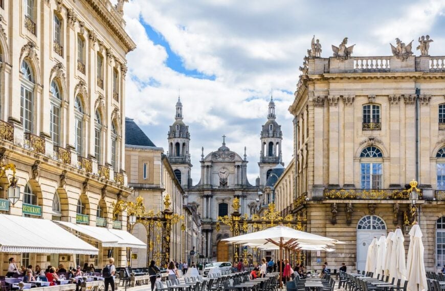 Nancy, France - September 12, 2019: Sunshine on the terrace of the sidewalk cafe of the Grand Hotel on the Stanislas square closed by a gilded wrought iron gate with Nancy cathedral in the background.