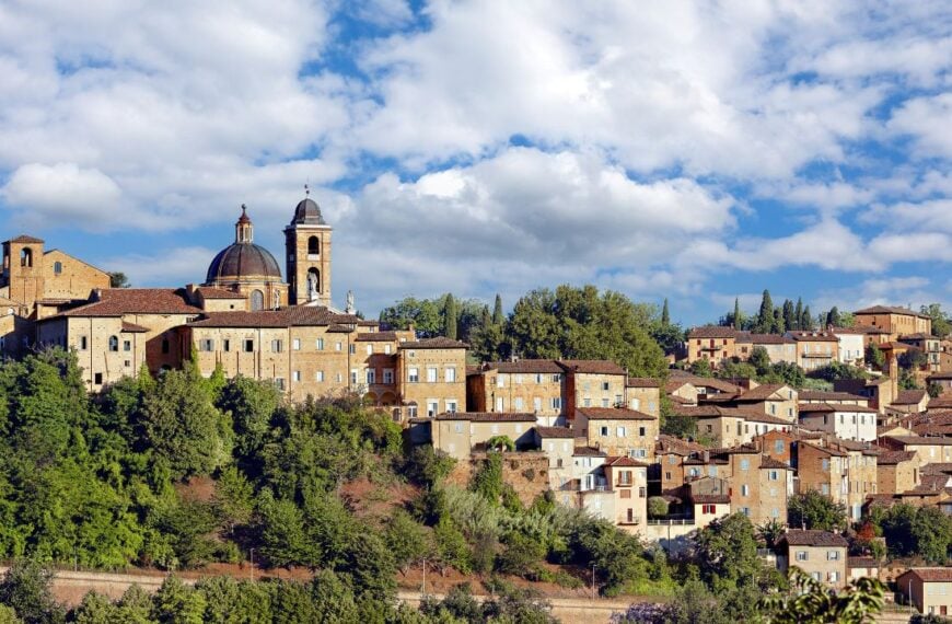 Palazzo Ducale stands majestically in Urbino, Italy, showcasing its medieval architecture against a backdrop of lush greenery and open skies, reflecting the city's storied past.