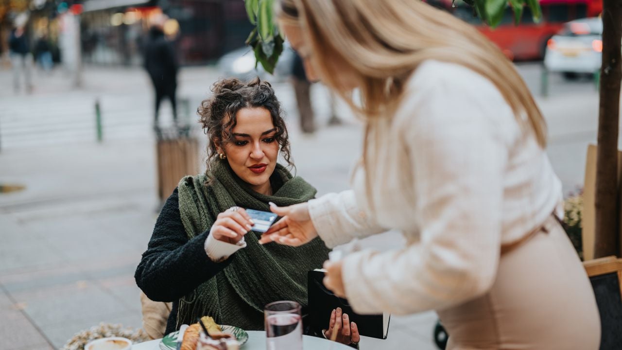 Woman handing credit card to waitress at a cozy outdoor cafe table during daylight.