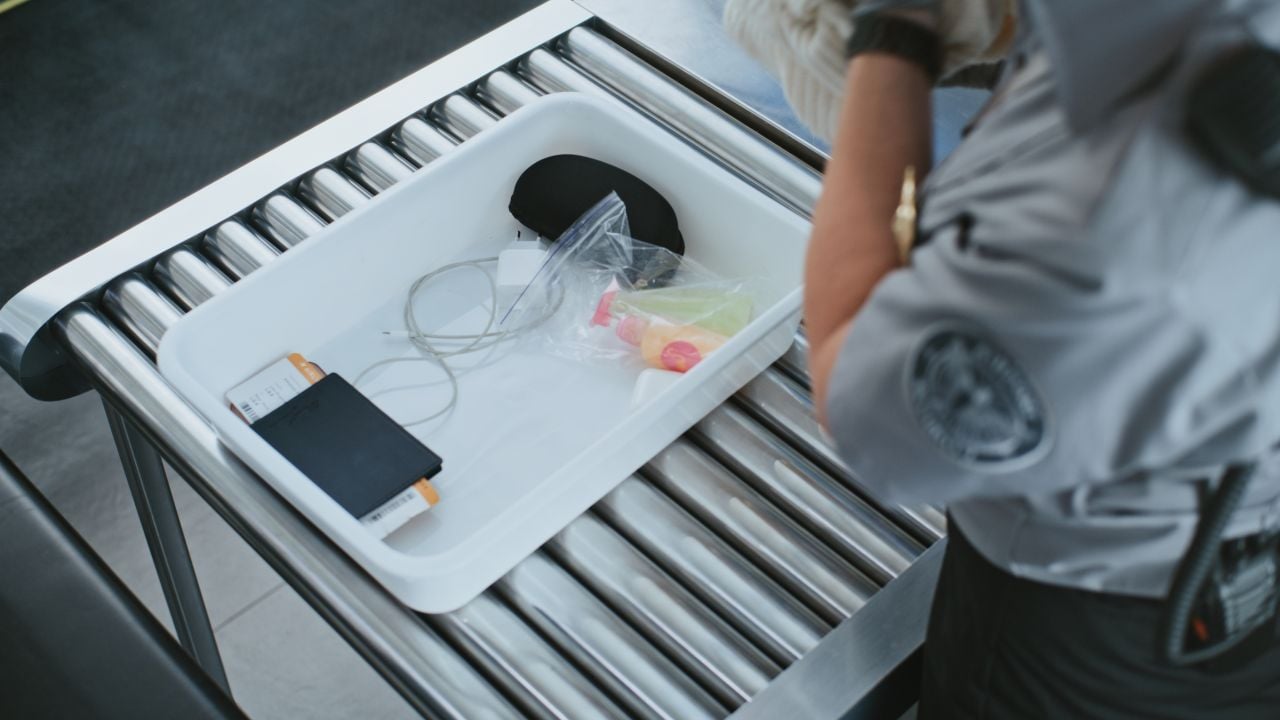 Airport security checkpoint with carry-on bags moving through an X-ray scanner.