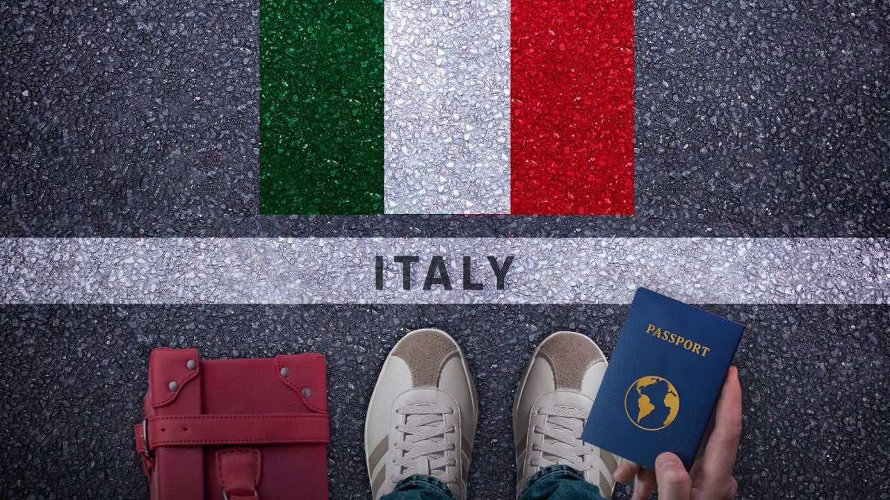 Traveler with bag, passport, and Italy flag on an asphalt road.