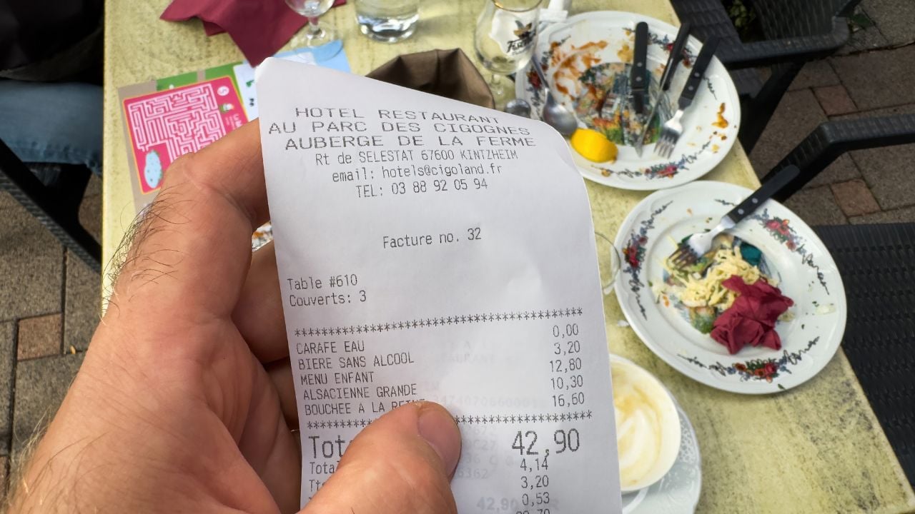Hand holding a restaurant receipt above a table after a meal in Sélestat, France.