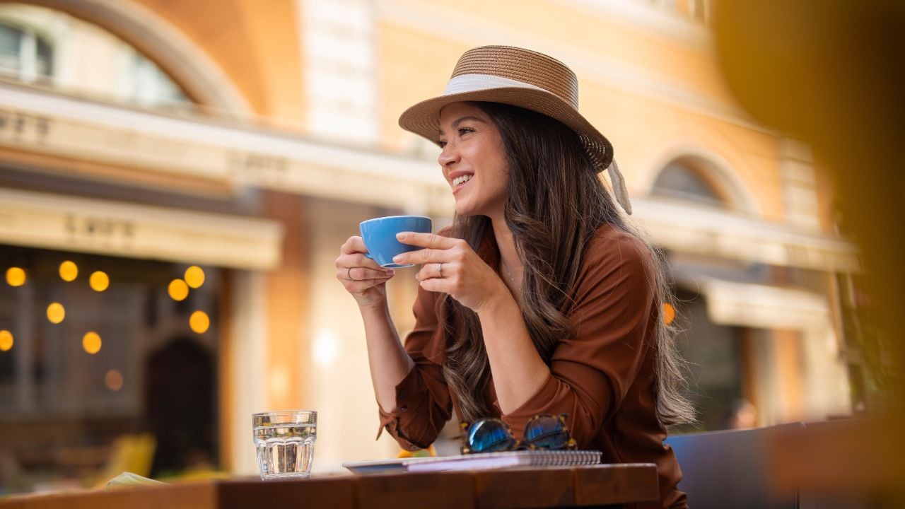 Stylish woman with a hat enjoying coffee at an outdoor café on a sunny day