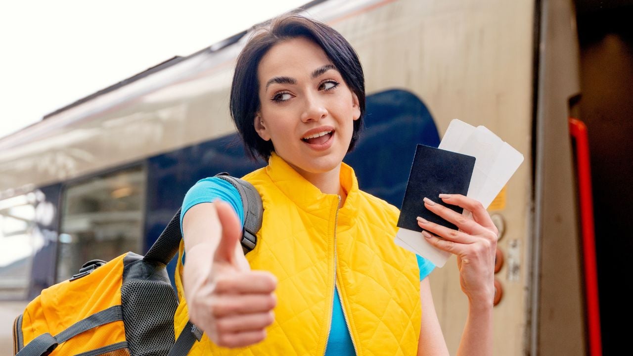 Woman holding train tickets and giving a thumbs up at a railway station.