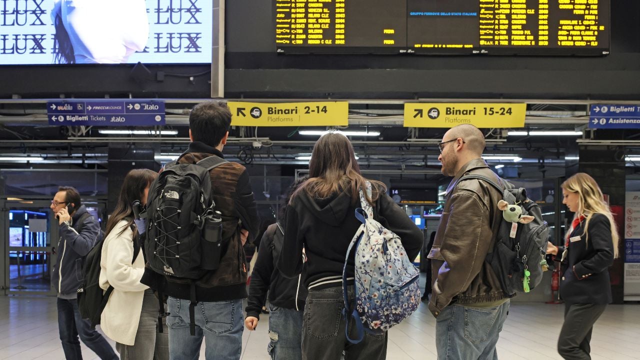Travelers looking at a departure board inside Naples Centrale station in Italy.
