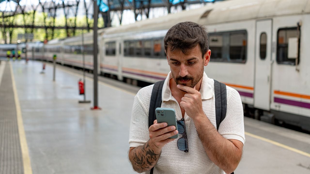 Traveler checking a smartphone while waiting at a busy train station.