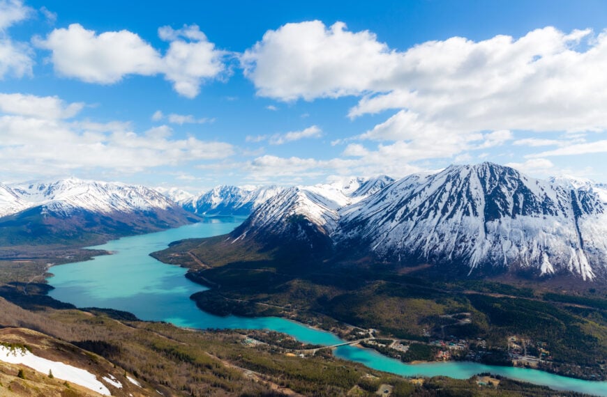 a turquoise lake winds through below snow capped mountains
