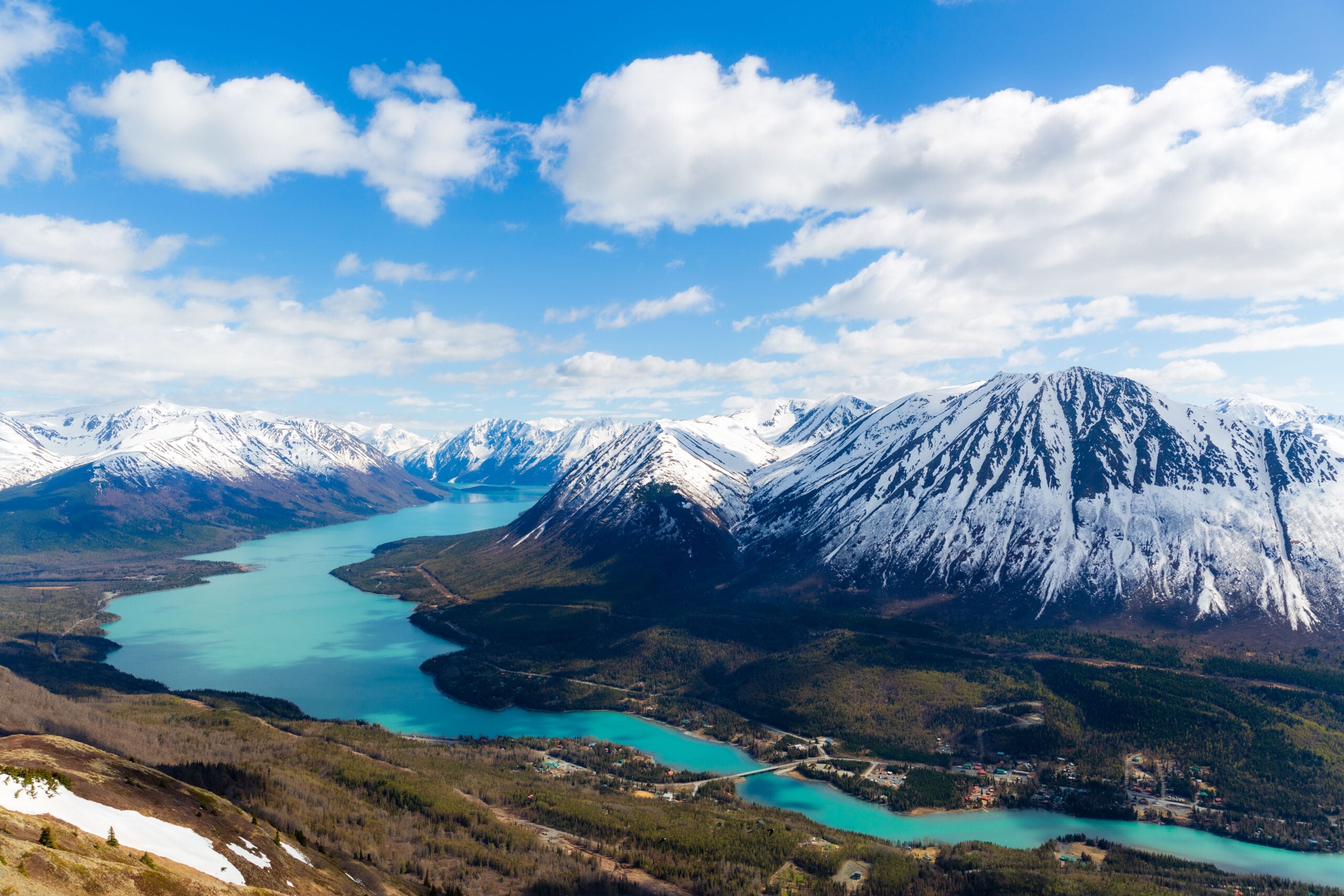 a turquoise lake winds through below snow capped mountains