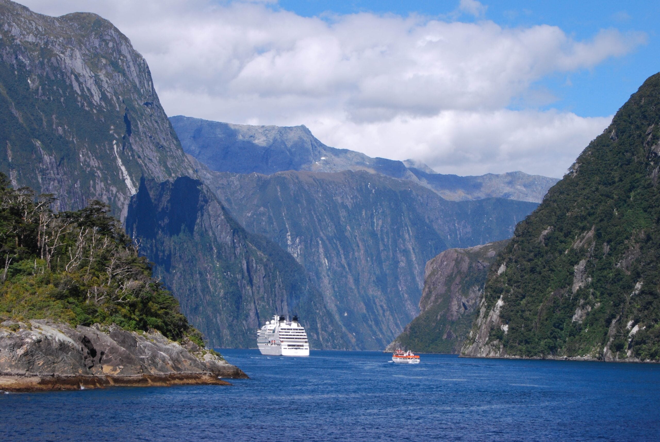 Milford Sound in Fiordland National Park, New Zealand, with cruise boat, steep cliffs, and cloud over the fiord