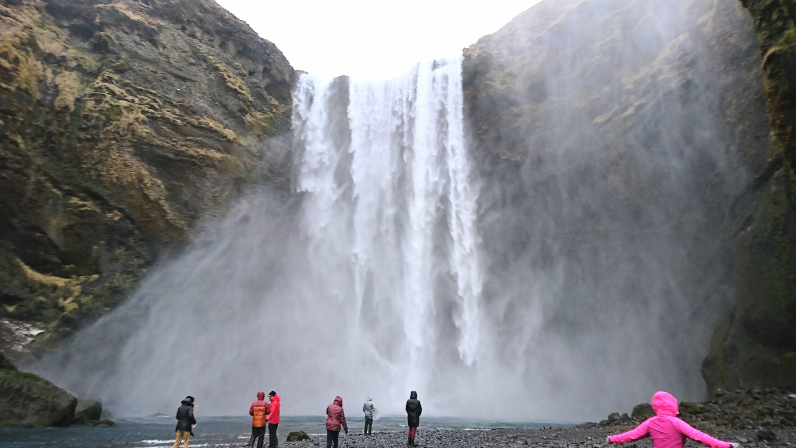 Skógafoss waterfall in Iceland with mist and visitors on a black pebble beach