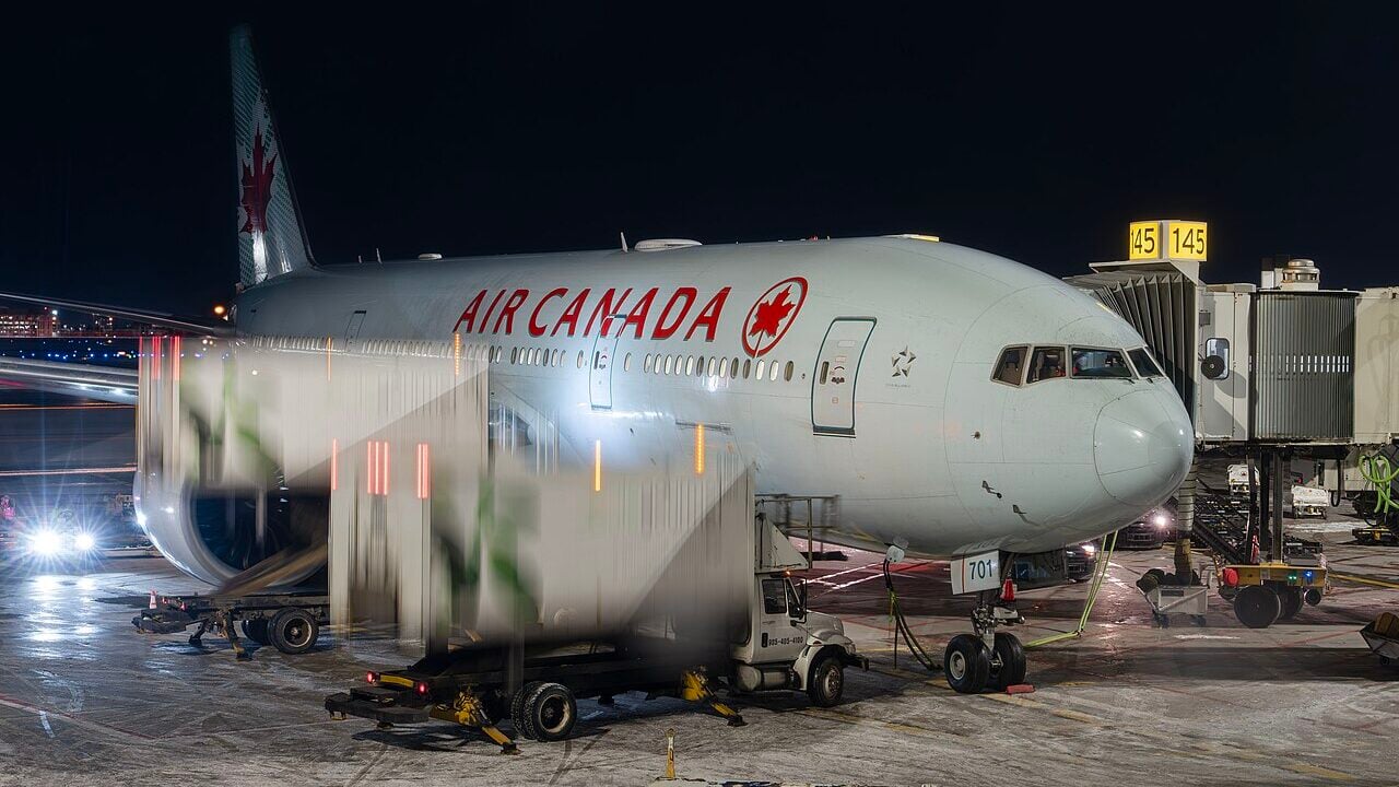 Air Canada Boeing 777-300ER (C-FIUA) at the gate at Toronto Pearson International Airport, with catering trucks positioning for loading.