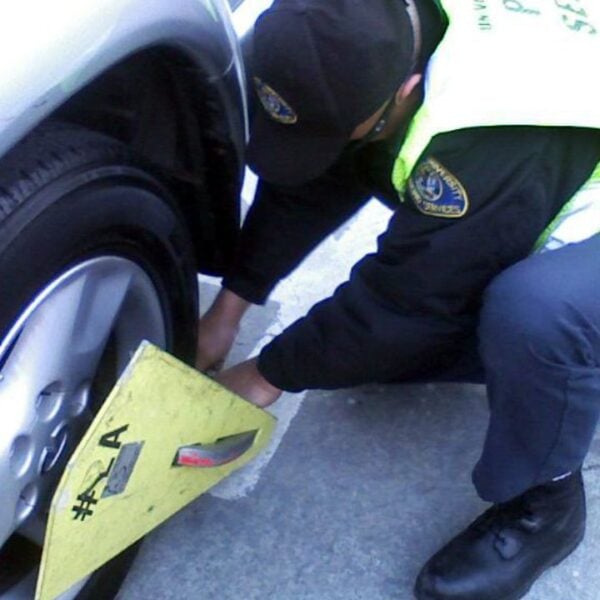 A parking enforcement officer clamps the wheel of a 2002 silver Infiniti Qx4 on the campus of San Jose State University in California.