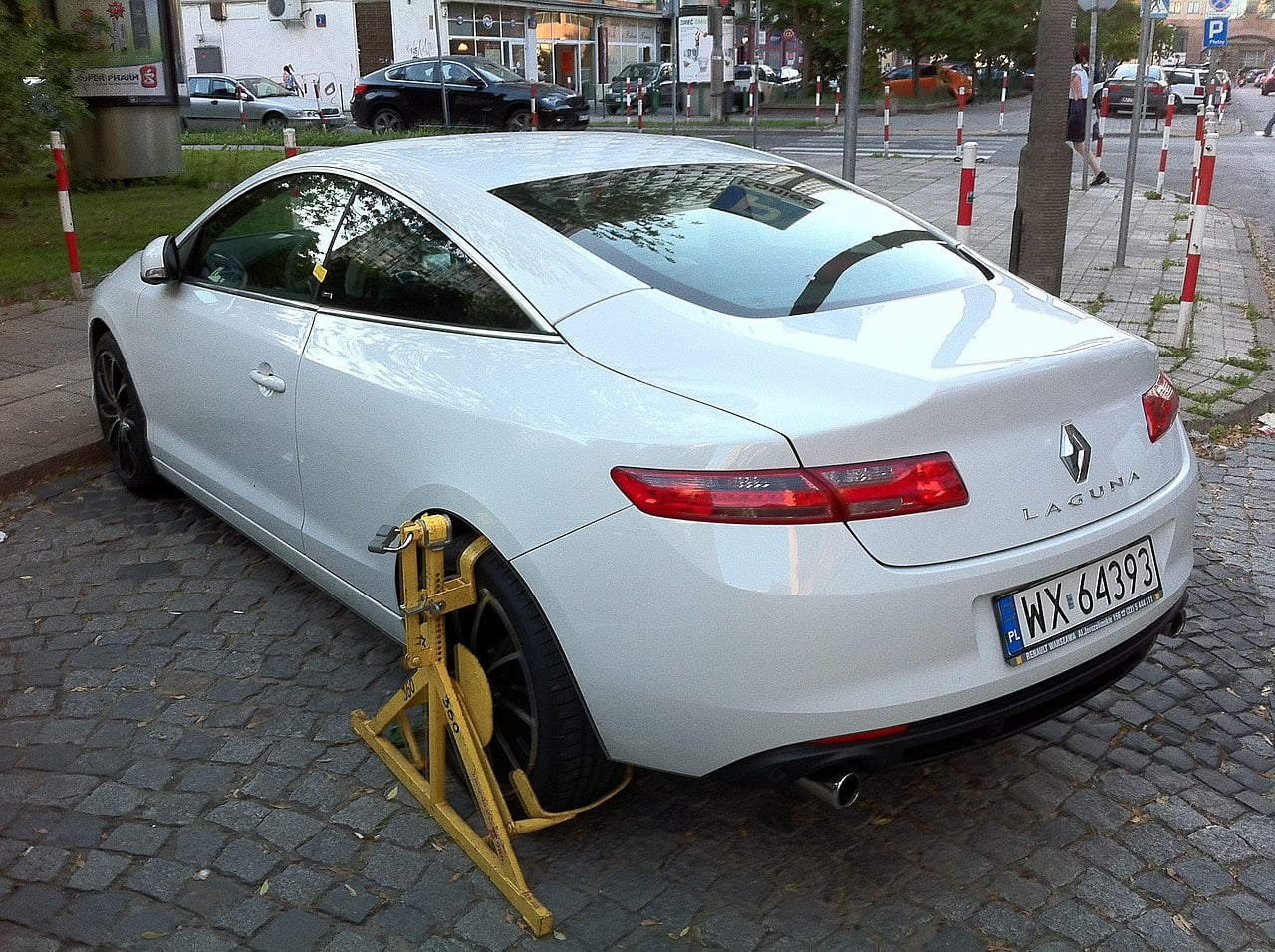 Rear left side view of a Renault Laguna III coupe with a parking violation wheel clamp. Picture taken on Ciepła street (facing north to Krochmalna) in Warsaw, Poland.