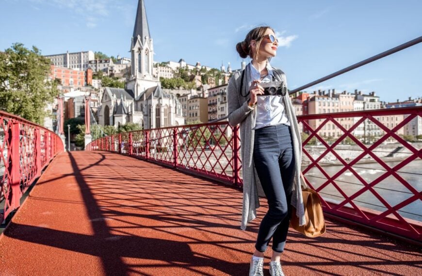 Stylish woman with photocamera enjoying morning city standing on the famous red footbridge in Lyon, France