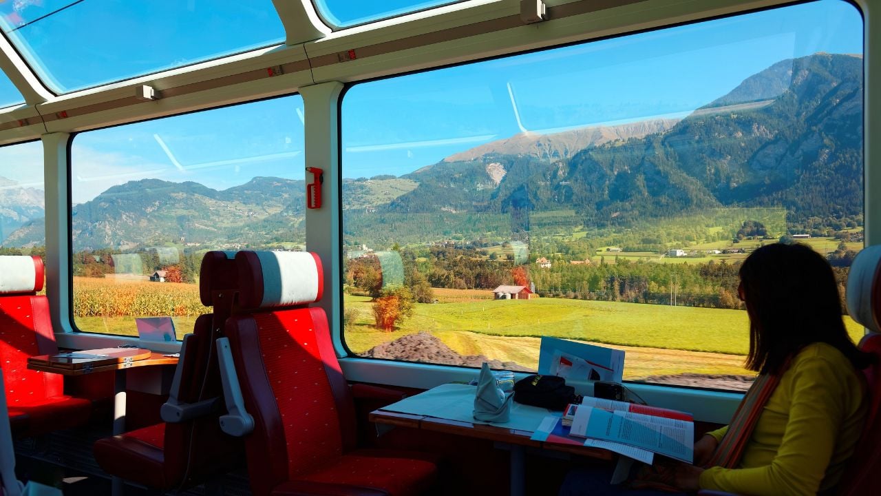 Passenger looking out of a train window at a scenic European landscape.