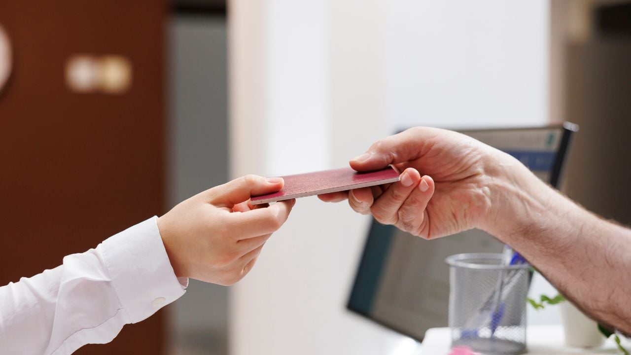 Traveler handing passport to hotel receptionist at check-in.