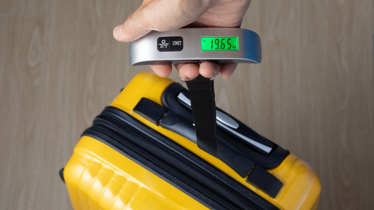 Traveler weighing luggage on a portable scale.