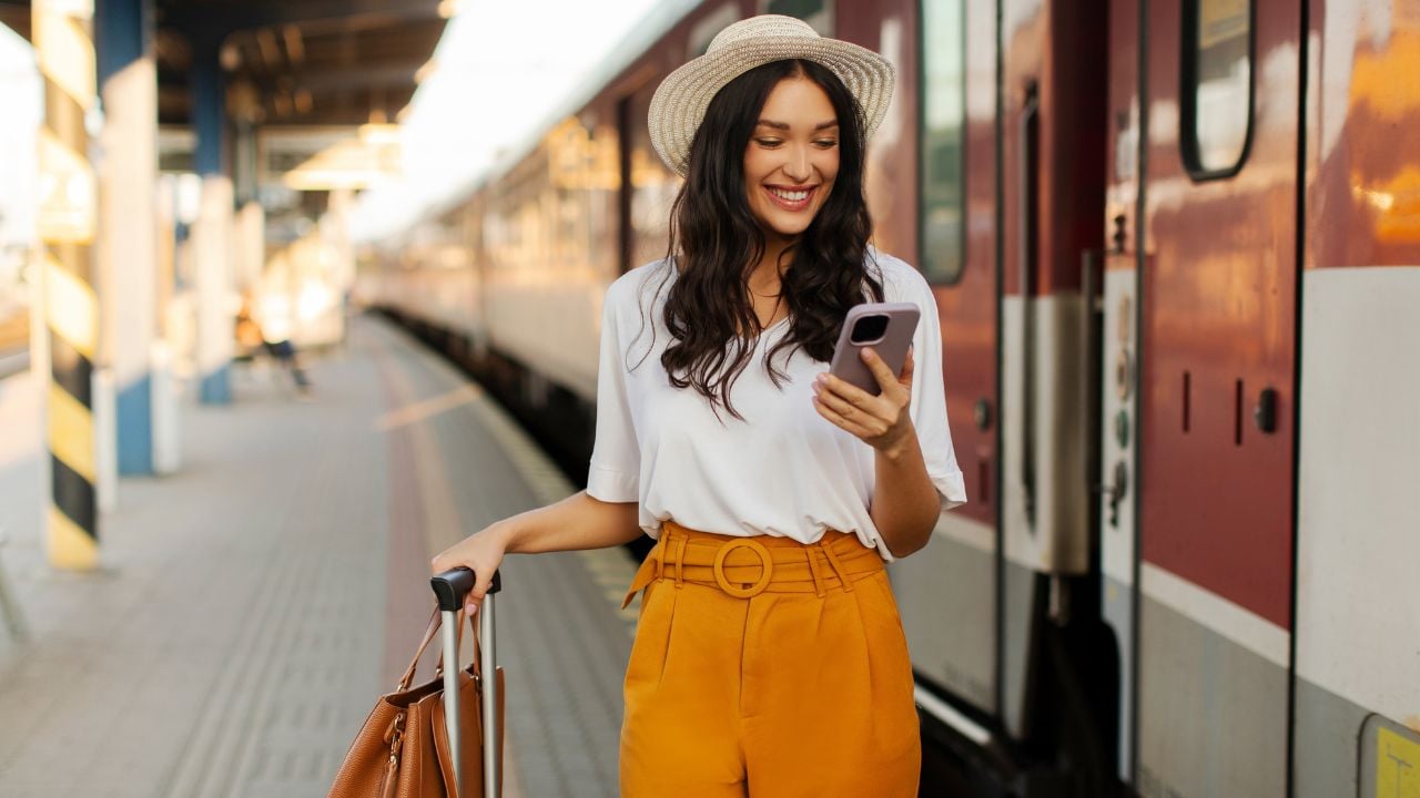 Traveler checking a phone beside a train at a railway platform.
