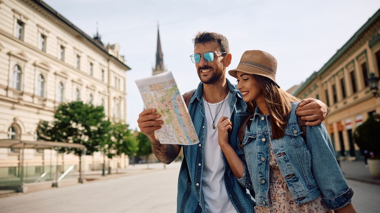 Happy couple of tourists reading map while walking through the city. Copy space.